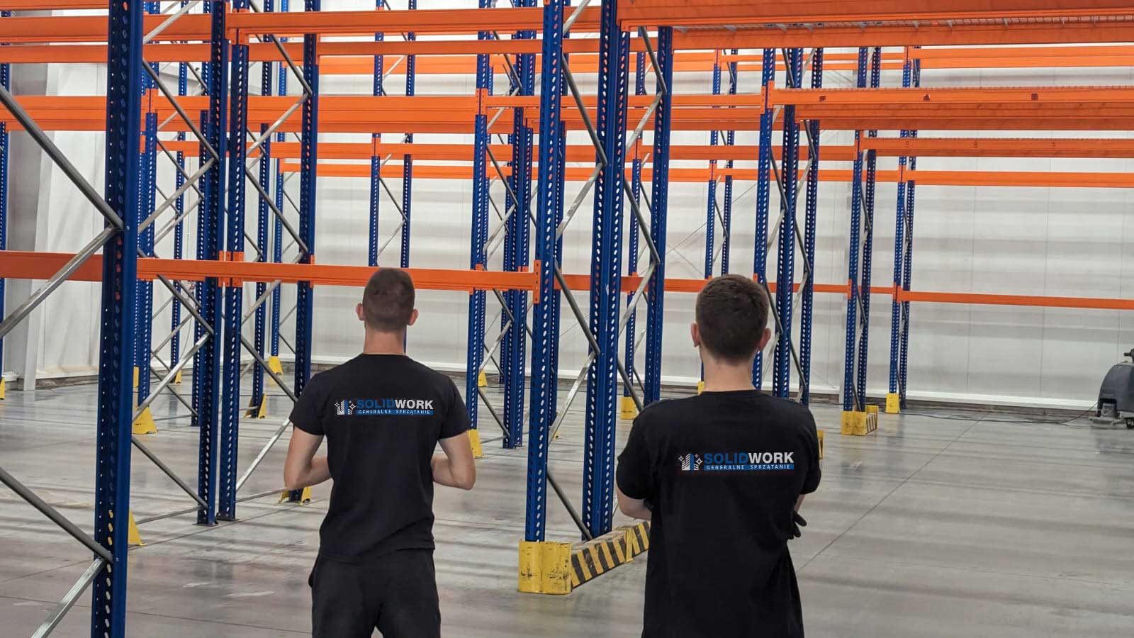 Pracownicy Solid Work stojący przy rusztowaniach w wielkim magazynie