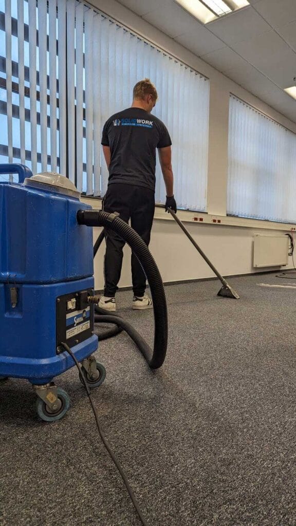 Pracownik Solid Work odkurzający wykładzinę w biurze