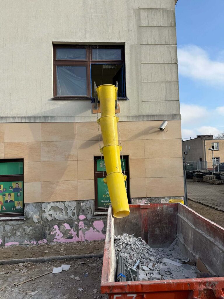 Opróżnianie obiektu z gruzu przy użyciu zsypu do kontenera. Prace demontażowe w budynku przed generalnym remontem wnętrza i elewacji